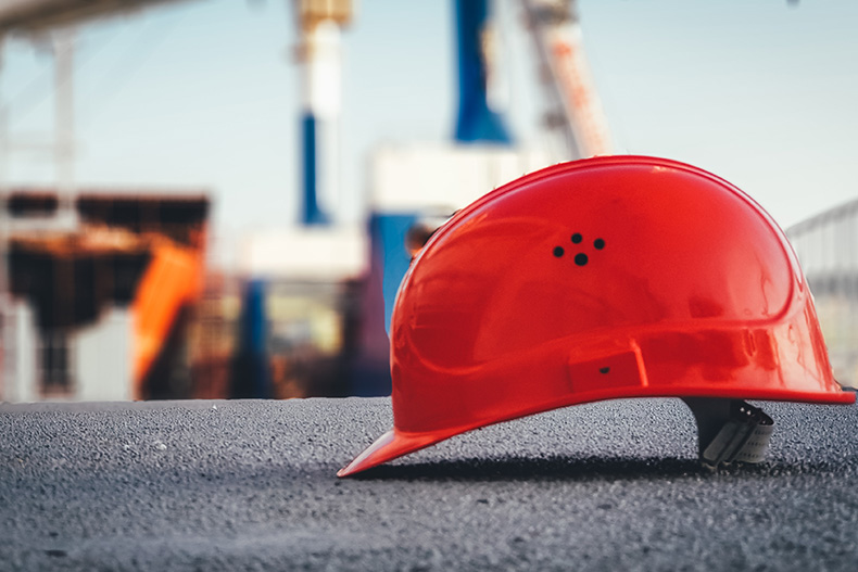 Ein roter Bauarbeiterhelm liegt auf dem Boden einer Baustelle.