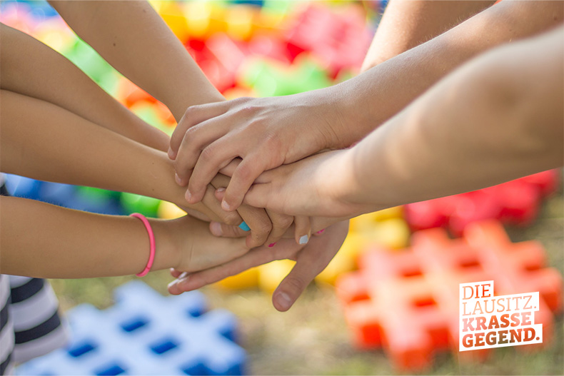 Mehrere Kinder legen ihre Hände übereinander als Zeichen für Teamgeist und Zusammenhalt
